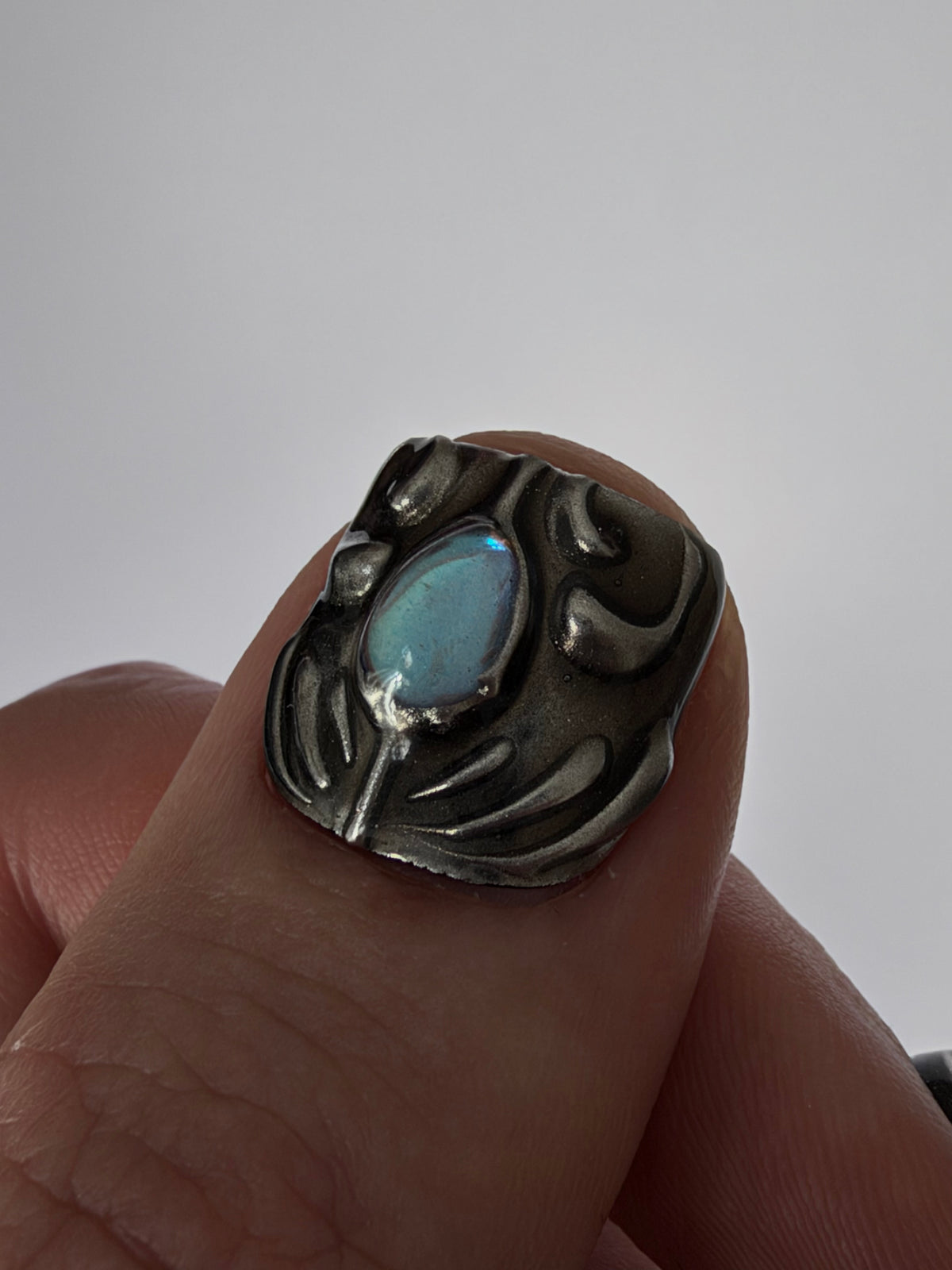 FORGED très court — Détail d’un pouce et de son cabochon bleu entouré de reliefs argentés