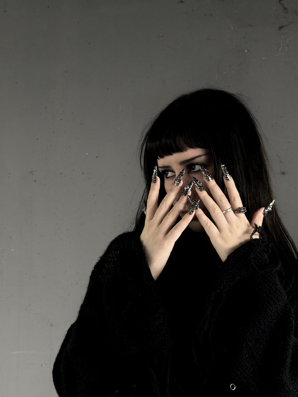 Zohra, l’artiste derrière AYUME, les mains devant le visage, ongles stiletto argentés.