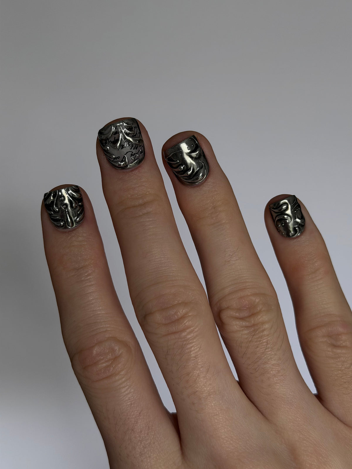 FILIGREE très court — Main portant les ongles très courts noirs et argentés, vue en biais