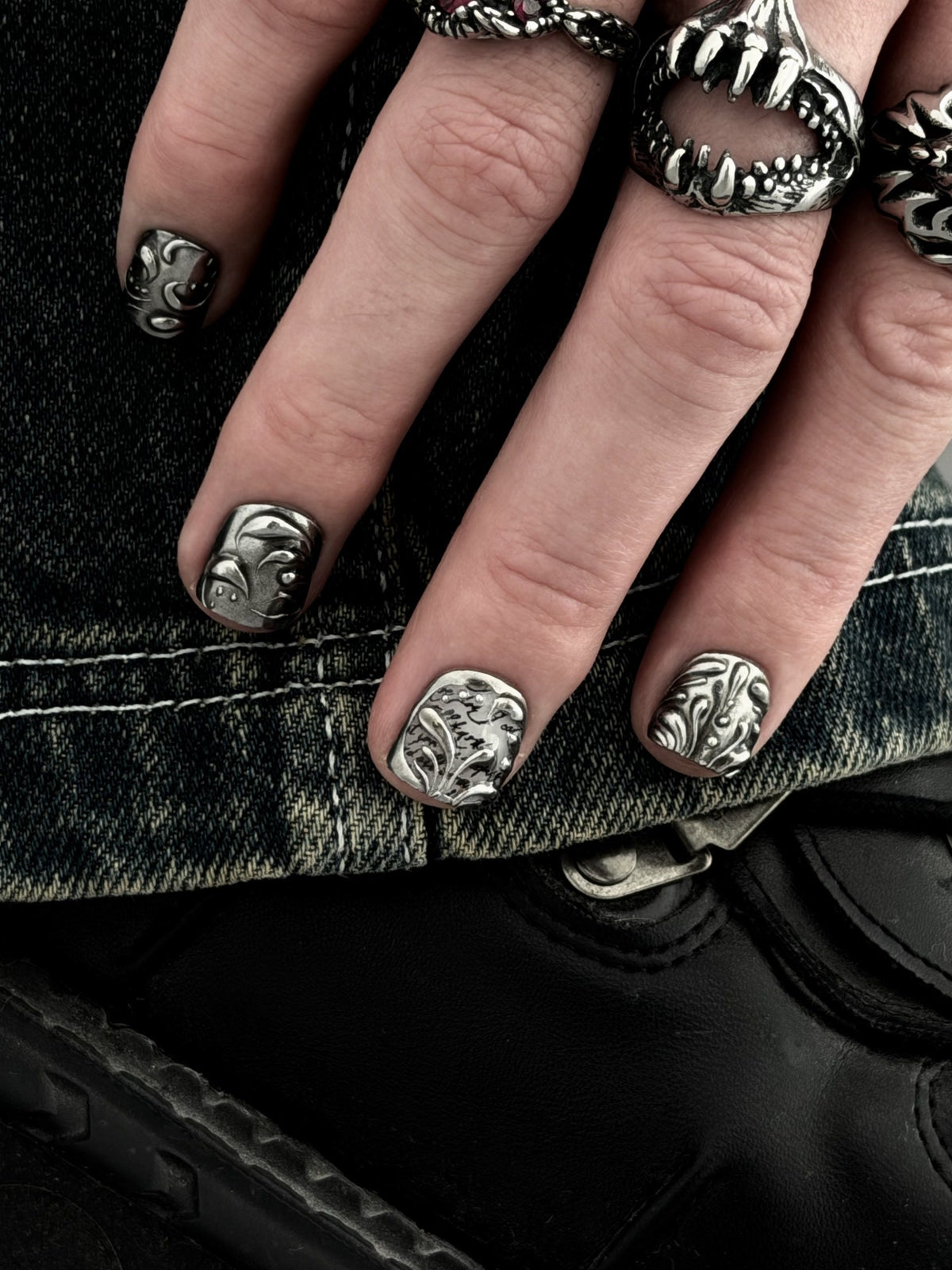FILIGREE très court — Main posée sur un denim, ongles très courts aux arabesques et à la calligraphie argentées