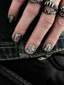 FILIGREE très court — Main posée sur un denim, ongles très courts aux arabesques et à la calligraphie argentées