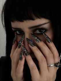 FORGED — Mains devant le visage, ongles Stiletto noirs et argentés aux cabochons bleus