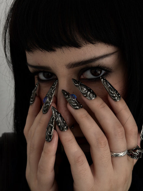 FORGED — Mains devant le visage, ongles Stiletto noirs et argentés aux cabochons bleus